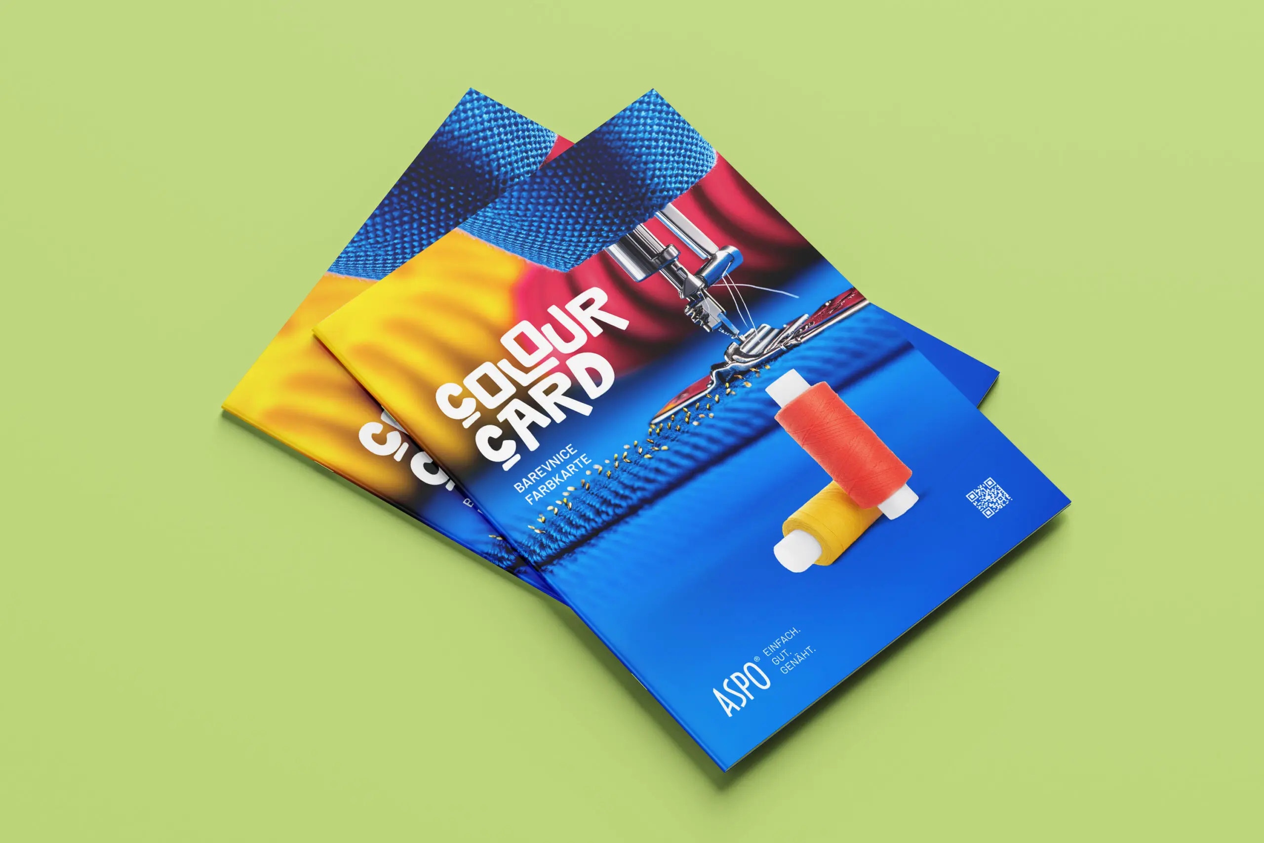 Zwei farbenfrohe Broschüren mit dem Titel „Colour Card“, auf denen Garnspulen und eine Nähnadel abgebildet sind, liegen auf einer hellgrünen Unterlage.