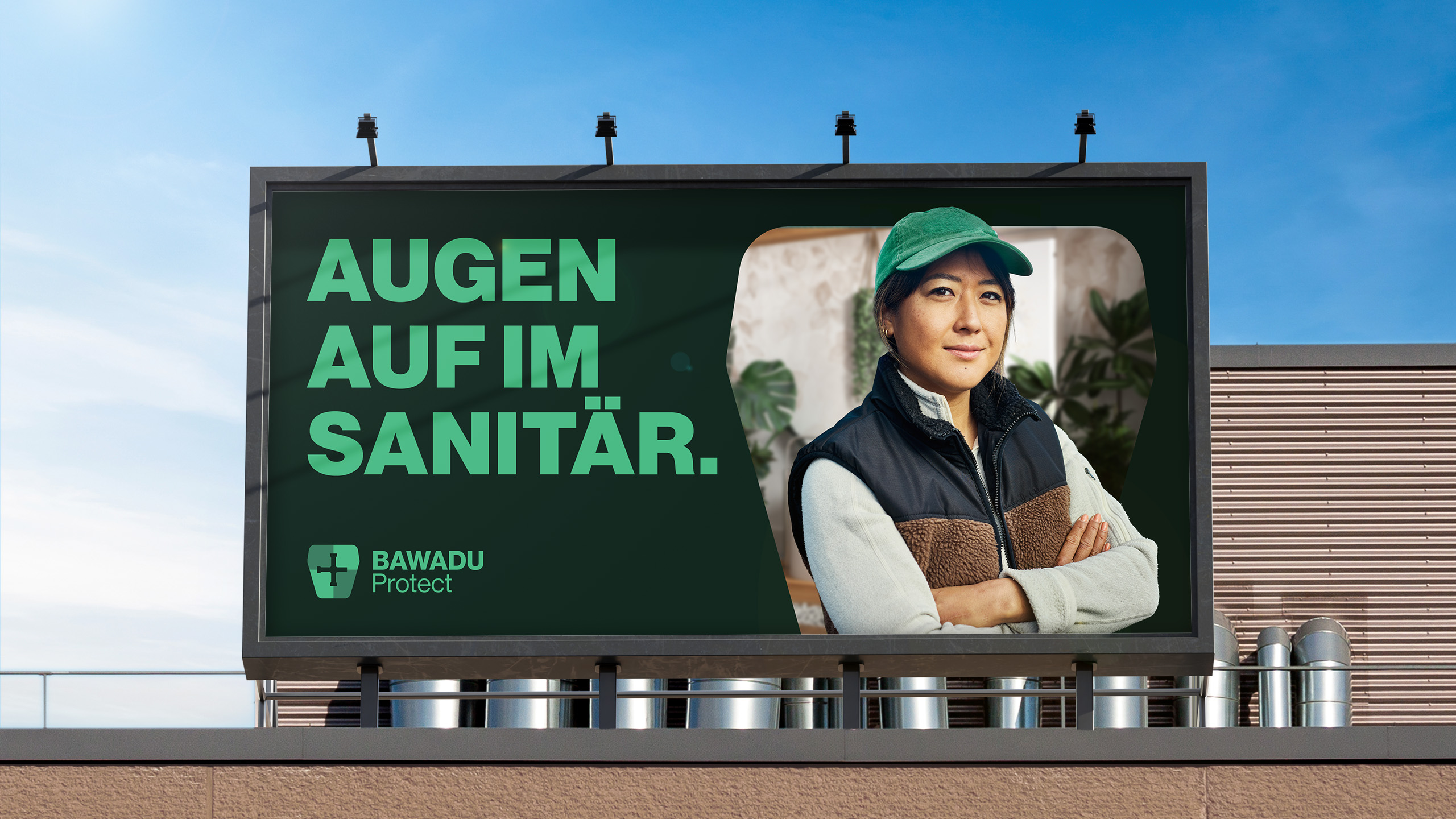 Auf einer Plakatwand ist eine selbstbewusste Frau in Outdoor-Kleidung mit verschränkten Armen zu sehen. Der Text lautet: „AUGEN AUF IM SANITÄR“. Neben ihr ist das Bawadu Protect-Logo zu sehen, im Hintergrund ein blauer Himmel.